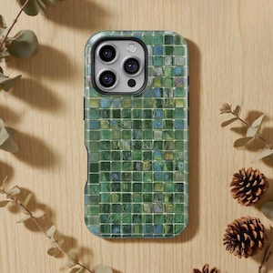 Könnte beinhalten: Eine Smartphone-Hülle mit einem Mosaikfliesen-Design in Grün-, Blau- und Grautönen. Die Hülle hat eine glänzende Oberfläche und einen schwarzen Rand. Die Handyhülle liegt auf einer hellbraunen Holzoberfläche.