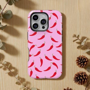 Puede incluir: Una funda de teléfono rosa con un patrón repetido de chiles rojos. La funda tiene un acabado brillante y un recorte para la cámara. El diseño es un accesorio divertido y vibrante para un teléfono móvil.