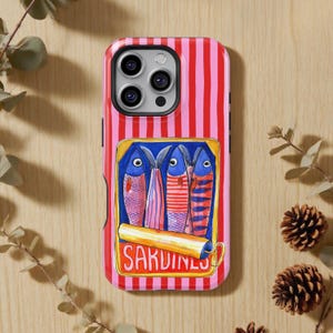 May include: A phone case with a pink and red striped background. The case features a rectangular image of four sardines in a can, with the word "SARDINES" printed on a yellow label. The sardines are blue, pink, and red.