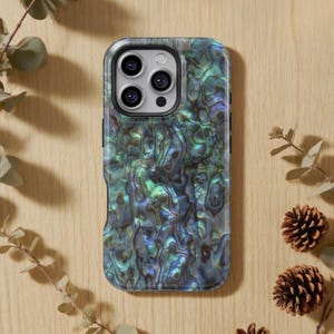 Op de afbeelding: Een smartphonehoesje met een parelmoer, iriserend ontwerp in tinten blauw, groen en grijs. De hoes heeft een zwarte rand en een camera-uitsparing. De telefoonhoes ligt op een lichtbruin houten oppervlak.