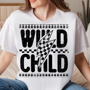 Puede incluir: Camiseta blanca con dise&ntilde;o gr&aacute;fico negro. El dise&ntilde;o presenta las palabras "WILD CHILD" con un rayo de bandera a cuadros. La camiseta tiene cuello redondo y mangas cortas.