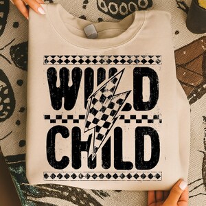 Puede incluir: Sudadera beige con la frase "WILD CHILD" en letras negras grandes y desgastadas. Un dise&ntilde;o de bandera a cuadros est&aacute; incorporado en un rayo gr&aacute;fico. La sudadera tiene cuello redondo y mangas largas.