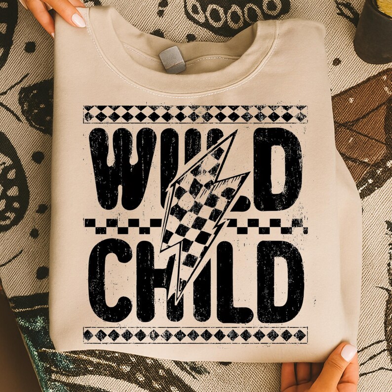 Puede incluir: Sudadera beige con la frase "WILD CHILD" en letras negras grandes y desgastadas. Un dise&ntilde;o de bandera a cuadros est&aacute; incorporado en un rayo gr&aacute;fico. La sudadera tiene cuello redondo y mangas largas.