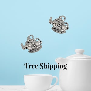 May include: Two silver-colored teapot charms with intricate detailing, each accompanied by a teacup and saucer. The charms are set against a light blue backdrop, with a white teapot and teacup in the foreground. The charms are approximately 1 inch in size.