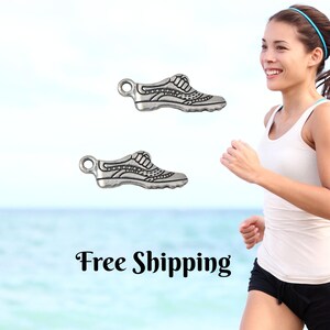 May include: Two silver-colored sneaker charms with detailed designs. The charms are small and have a loop at the top for attaching to a bracelet or necklace. The background shows a woman running near the ocean. Text in the image says "Free Shipping".