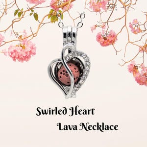 May include: A silver-colored necklace with a heart-shaped pendant. The pendant features a pink lava stone and is embellished with clear crystals. The necklace is suspended from a delicate chain. The text "Swirled Heart Lava Necklace" is below the necklace.