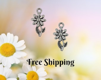 May include: Two silver-colored daisy flower charms with leaves and a loop for hanging. The charms are set against a soft, blurred background with white and yellow daisies. The image also contains the text "Free Shipping".