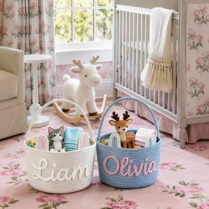 Puede incluir: Dos cestas de cuerda, una blanca y otra azul, sobre una alfombra floral. La cesta blanca, con la etiqueta "Liam", contiene un gato de peluche y orejas de conejo. La cesta azul, con la etiqueta "Olivia", contiene una figura de ciervo. Un ciervo balancín y una cuna en el fondo.