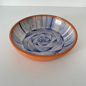 May include: A small, round ceramic bowl with a vibrant orange exterior and a blue and white spiral design on the interior. The bowl's interior features a hand-drawn spiral pattern, creating a unique and artistic aesthetic.