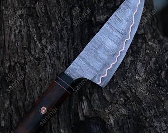 May include: A fixed-blade knife featuring a patterned Damascus steel blade with a prominent wavy copper inlay along the edge. The handle is crafted from dark brown wood with black accents, secured by a decorative circular mosaic pin near the bolster.