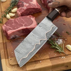 May include: A kitchen knife with a Damascus steel blade featuring a wavy copper inlay, a dark wooden handle, and a copper bolster. The blade has a distinct layered pattern, and the knife is held at an angle, showcasing its sharp edge and design.