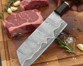 May include: A kitchen knife with a Damascus steel blade featuring a wavy copper inlay, a dark wooden handle, and a copper bolster. The blade has a distinct layered pattern, and the knife is held at an angle, showcasing its sharp edge and design.