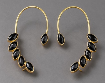 May include: A pair of gold ear cuffs featuring a curved metal wire frame adorned with five marquise-cut black stones arranged in a cascading row, with a single matching black stone at the opposite end of the wire arch.