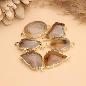 May include: A collection of six irregular, polished agate stone connectors, each featuring natural brown and beige banding. Every stone is encased in a bright gold-toned metal rim and includes two small circular loops on opposite sides.
