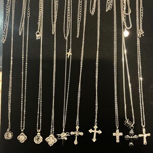 Peut inclure: Présentation de colliers en argent avec divers pendentifs, notamment des croix, des cœurs et des formes géométriques. Les colliers sont suspendus sur un fond noir, mettant en valeur les différents styles et longueurs de chaînes.