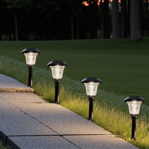 Könnte beinhalten: Vier schwarze Solar-Wegeleuchten beleuchten einen Steinweg und eine Rasenfläche. Jede Leuchte hat einen dekorativen, strukturierten Glasschirm und eine dunkle Kappe, die abends ein warmes Leuchten erzeugt.