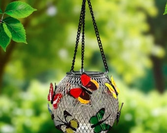May include: A hanging solar-powered lantern with a silver wire mesh design. The lantern is adorned with colorful butterfly decorations in red, yellow, and green. It hangs from a black chain against a blurred green background.