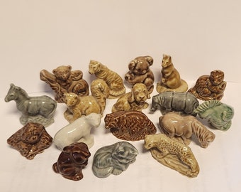 May include: A collection of 16 ceramic animal figurines, including a zebra, a tiger, a hippopotamus, a leopard, a monkey, a rabbit, a cat, a dog, and a koala. The figurines are painted in various shades of brown, green, and gray.