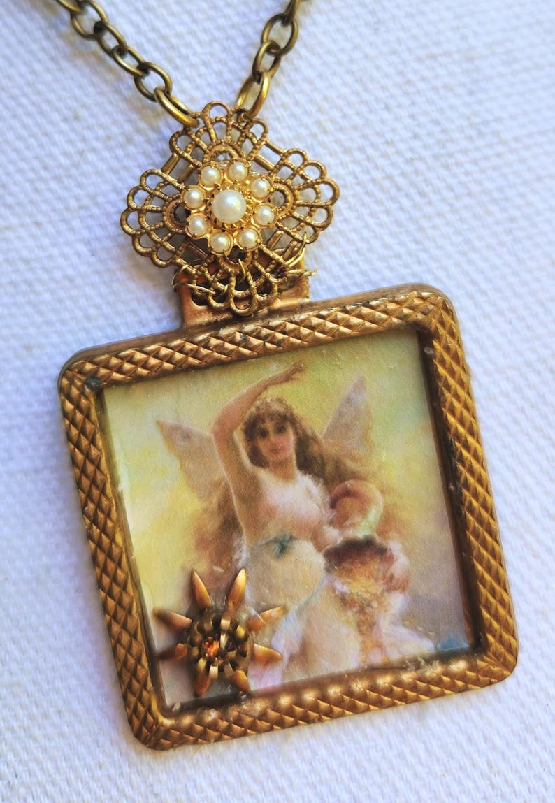 May include: A vintage gold-toned pendant necklace. The pendant features a rectangular frame with a detailed image of a woman with wings. The frame is adorned with a star and a decorative top with pearls. The chain is also gold-toned.