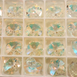 May include: A clear plastic container with 12 iridescent heart-shaped crystal charms. The charms are arranged in rows and columns.