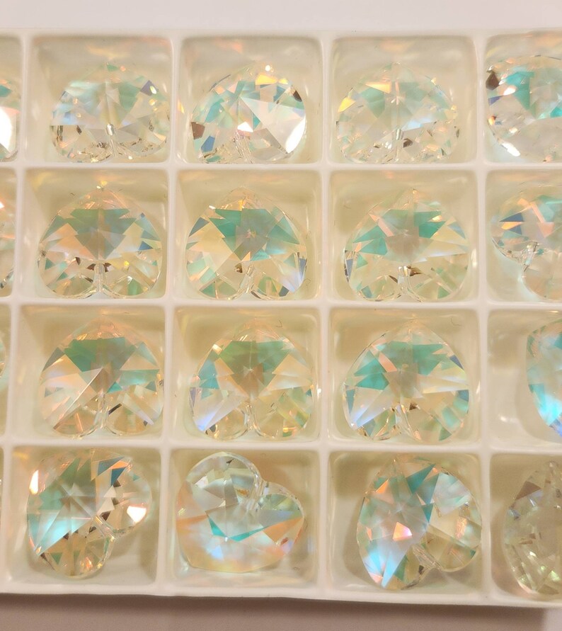 May include: A clear plastic container with 12 iridescent heart-shaped crystal charms. The charms are arranged in rows and columns.