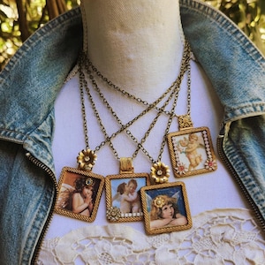 May include: A collection of antique-style necklaces featuring square pendants with cherub artwork. The pendants are framed in gold-colored metal and hang from delicate chains. Each necklace has a unique cherub image.