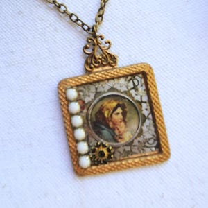 May include: Vintage-style square pendant necklace with a gold-tone frame. The pendant features a portrait of a woman, white beads, and a decorative floral design. The necklace has a delicate chain.