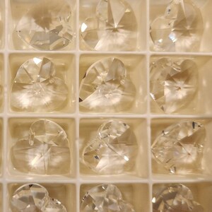 May include: A clear plastic container filled with 18 crystal heart-shaped charms. The charms are arranged in a grid pattern.