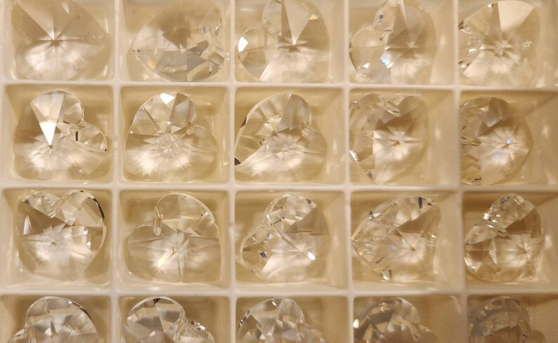 May include: A clear plastic container filled with 18 crystal heart-shaped charms. The charms are arranged in a grid pattern.