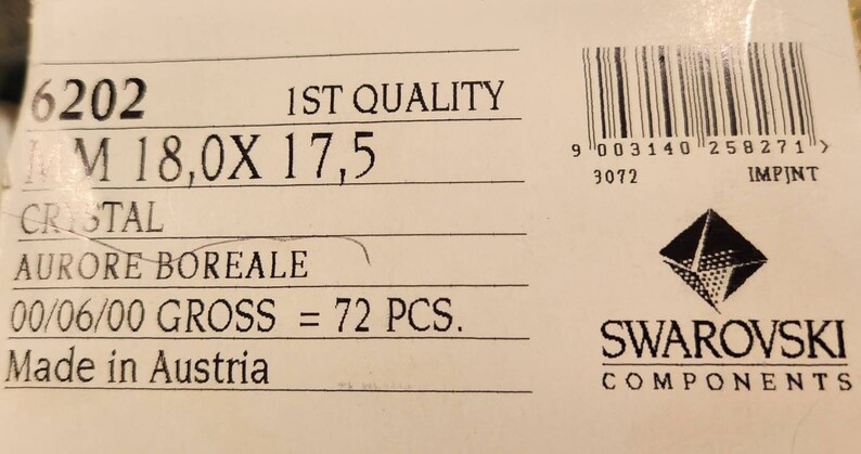 May include: A white label with black text that reads "6202 1ST QUALITY M 18,0X 17,5 CRISTAL AURORE BOREALE 00/06/00 GROSS = 72 PCS. Made in Austria" and a barcode with the text "9 003140 258271 > 3072 IMPINT" below it. The label also features a black and white Swarovski logo with the text "SWAROVSKI COMPONENTS".