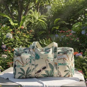 May include: A rectangular duffel bag featuring a cream-colored fabric with a repeating pattern of leopards, flamingos, toucans, and tropical palm leaves in shades of green, orange, and black, complete with two matching fabric handles.