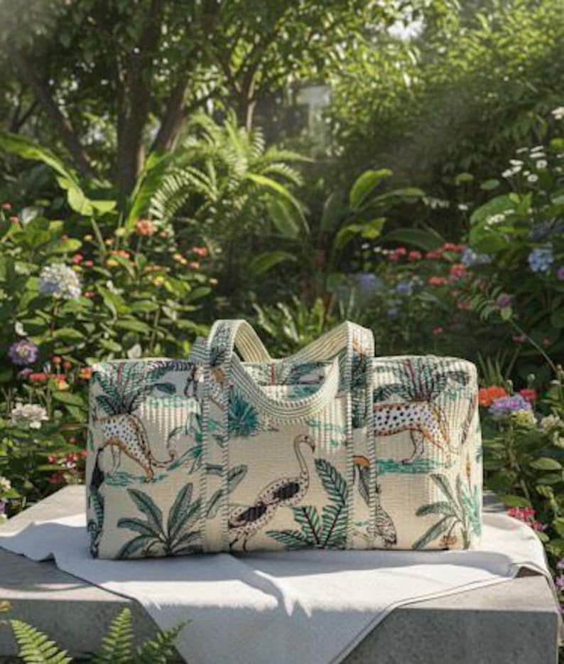 May include: A rectangular duffel bag featuring a cream-colored fabric with a repeating pattern of leopards, flamingos, toucans, and tropical palm leaves in shades of green, orange, and black, complete with two matching fabric handles.