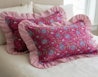 May include: Two decorative throw pillows with a vibrant pink floral pattern and ruffled edges. The pillows feature a repeating design of blue and white flowers with green leaves. The ruffled edges are striped in red and white.