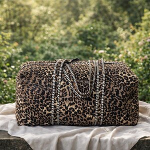 May include: A rectangular duffel bag featuring a brown and black leopard print pattern. The bag includes two long, sturdy carrying handles with a distinct black and white striped design that extends down the front of the bag's main body.