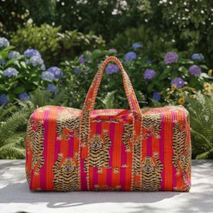 May include: A rectangular duffel bag featuring a vibrant pattern of orange and pink vertical stripes overlaid with repeating illustrations of tigers in black, white, and yellow. The bag has two matching fabric handles on top.