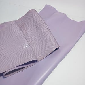 K&ouml;nnte beinhalten: Zwei Bl&auml;tter lavendelfarbenes Leder. Ein Blatt ist glatt und flach, w&auml;hrend das andere gefaltet und mit einem schuppenartigen Muster strukturiert ist. Das Leder wird wahrscheinlich f&uuml;r Bastelarbeiten oder Mode verwendet.