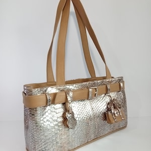 May include: Silver handbag with a snakeskin pattern, tan leather straps, and decorative buckles. The bag has a rectangular shape with a top handle design. A small, matching purse charm hangs from the front.