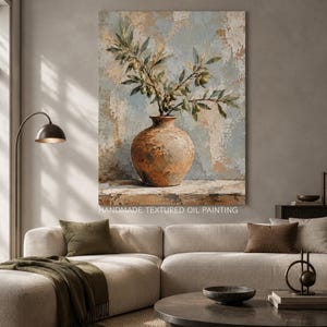 Puede incluir: Una pintura al óleo texturizada sobre lienzo que representa una rama de olivo con hojas verdes y pequeñas aceitunas dentro de un jarrón de cerámica redondo, rústico y de color terracota. El fondo presenta un acabado desgastado en tonos azul y beige.
