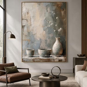 Puede incluir: Una pintura al óleo vertical con un fondo abstracto texturizado en tonos azul, beige y marrón. La obra representa un bodegón con dos cuencos pequeños y un jarrón alto que contiene delicadas flores blancas sobre una superficie.