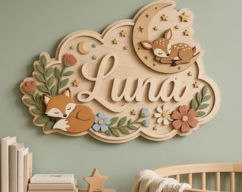 May include: A wooden wall sign featuring the name Luna in script lettering, decorated with a sleeping deer on a crescent moon, a sleeping fox, small stars, and various floral elements in muted tones of brown, green, blue, and cream.