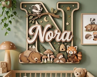 May include: A large, layered wooden wall sign shaped like the letter N, featuring the name Nora in white script. The design includes woodland elements like a badger, a sleeping bear, a red panda, hedgehogs, mushrooms, and a beehive in earth tones.