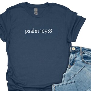 May include: A navy blue t-shirt with the text "psalm 109:8" in white. The shirt is paired with light blue denim jeans. The clothing is displayed on a white background.