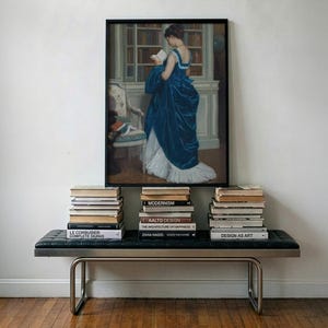 Pu&ograve; includere: Una stampa incorniciata di un dipinto che raffigura una figura in un abito di velluto blu intenso che legge un libro in una biblioteca, sopra una panca in pelle nera trapuntata con telaio in metallo e tre pile di libri come Modernism.