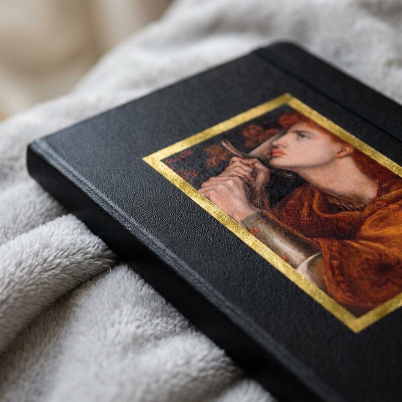 May include: A black hardcover journal featuring a rectangular inset print of a classical painting depicting a person with reddish hair holding a sword. The artwork is framed by a thin gold border, and the journal cover has a textured, matte finish.
