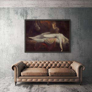 May include: A framed oil painting depicting a reclining figure draped in white fabric, positioned above a tufted tan leather sofa. The artwork features dark, moody tones with a central illuminated subject, hanging on a textured grey concrete wall.
