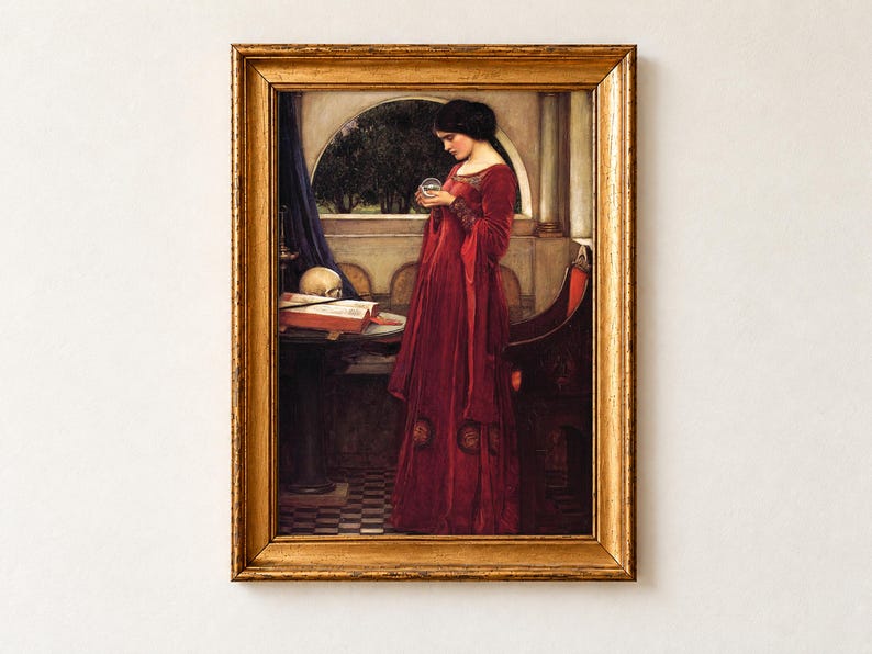 The Crystal Ball by John William Waterhouse, 1902, as a framed print in an antique gold frame on a cream wall. A dark-haired woman in a red velvet gown gazes into a crystal ball, a skull resting on an open book of spells on the table beside her.