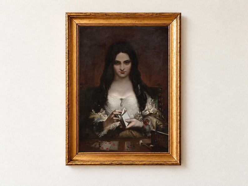 The Wish by Theodor von Holst, 1840, as a framed print in an antique gold frame on a cream wall. A pale woman with long black hair and a lace shawl shuffles a deck of playing cards, more cards and an open jewellery box on the table before her.
