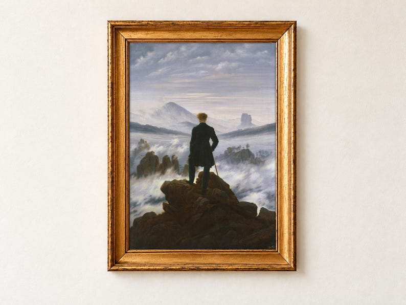 Wanderer Above the Sea of Fog by Caspar David Friedrich, 1818, as a framed print in an antique gold frame on a cream wall. A man in a dark green coat stands with his back to us on a rocky summit, leaning on a cane and gazing over a sea of fog towards distant mountains.