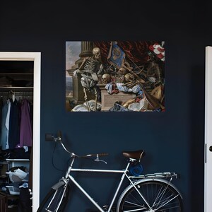 May include: A silver bicycle with a brown seat and a rear rack is positioned in front of a wall displaying a rectangular print of a vanitas painting featuring a skeleton, skulls, armor, musical instruments, and books.