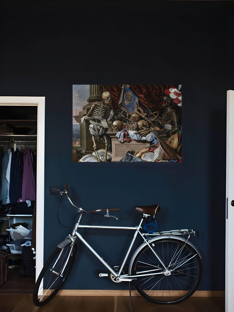 May include: A silver bicycle with a brown seat and a rear rack is positioned in front of a wall displaying a rectangular print of a vanitas painting featuring a skeleton, skulls, armor, musical instruments, and books.